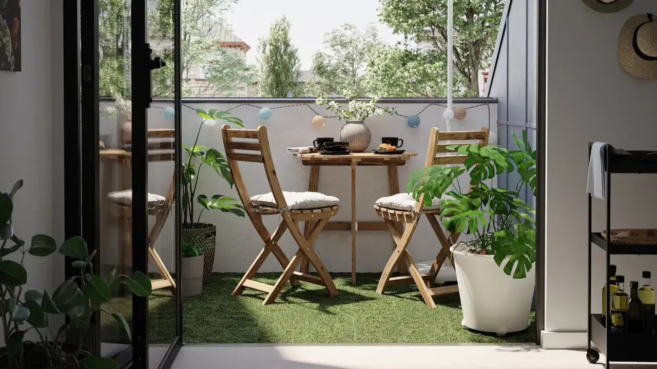 Drewniany stolik i krzesła na sztucznej trawie, idealne, by osłonić balkon w bloku. Rośliny dodają uroku.